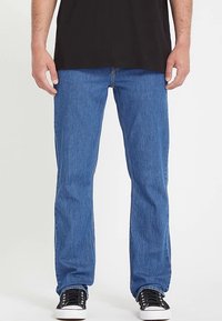 Jeans in denim blu con taglio a gamba dritta, caratterizzati da un classico design a cinque tasche, dettagli cuciti e indossati con sneakers nere.