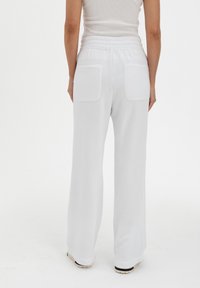 White sweatpants with a loose fit, elastic waistband, and two back pockets. Soft texture, plain design, and straight leg shape.