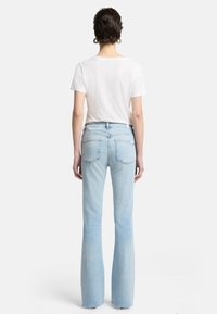 Jeans svasati azzurro chiaro con un finish sbiadito, caratterizzati da un classico design a cinque tasche e tasche posteriori cucite, indossati con una t-shirt bianca.