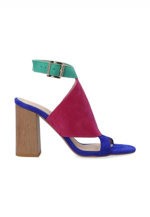 Sandale à talons multicolore avec un upper en suede rose, une sangle de cheville verte et une sangle de orteil bleue. Un talon en bois bloc complète le design.
