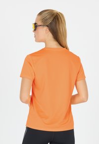 Kortärmad orange skjorta i mjukt tyg, med rund hals och en figurnära design, tillsammans med svarta byxor.