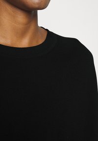 Černý pletený svetr s žebrovaným kulatým výstřihem a měkkou texturou, který zdůrazňuje materiál a detaily designu při detailním pohledu.