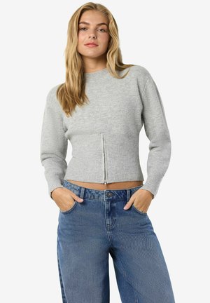 Suéter recortado gris claro con cuello redondo y cierre frontal; dobladillo acanalado y mangas largas. Combinado con jeans de mezclilla azul de talle alto.