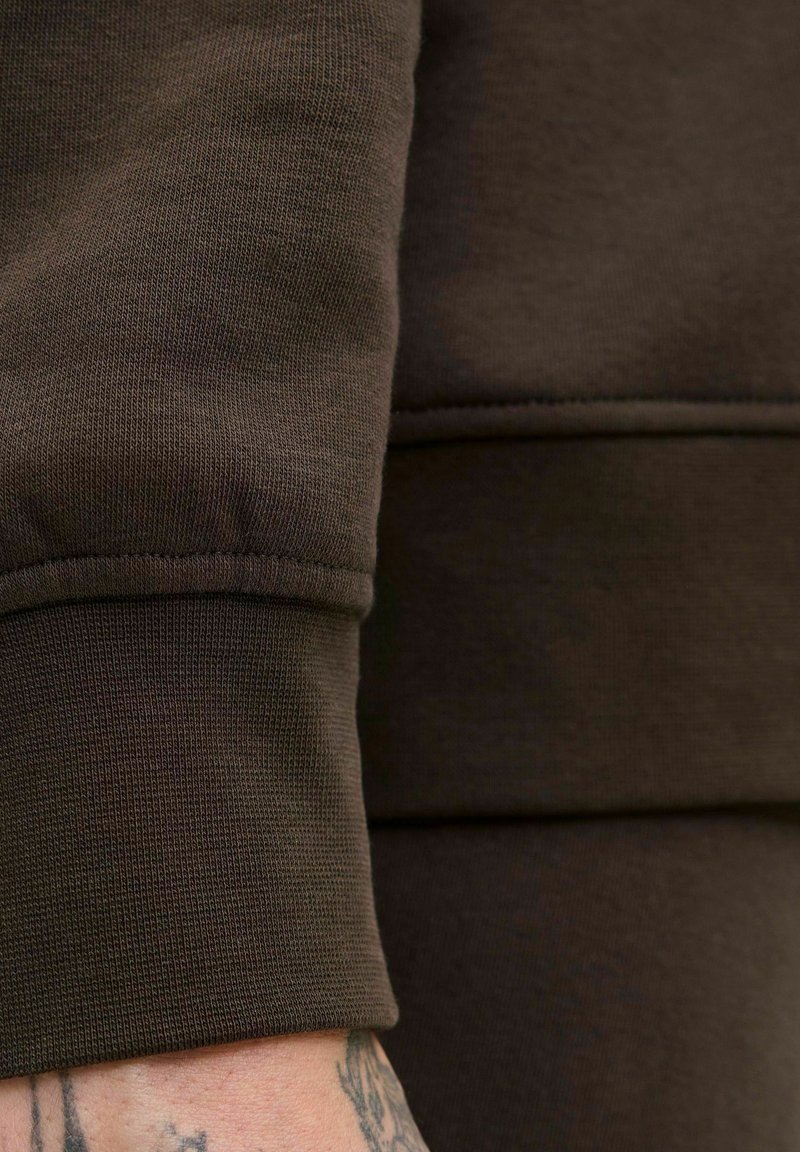 Brauner Baumwoll-Sweatshirtstoff mit gerippten Bündchen und strukturiertem Finish. Sichtbare Nahtdetails und eine Nahaufnahme des Ärmelbereichs.