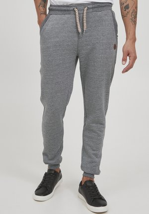 Gray jogger pants with textured fabric, elastic waist, and rope drawstring. Features side pockets and a contrasting logo detail.