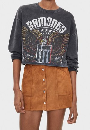 Sweatshirt noir court avec un design graphique représentant un aigle et un bouclier, associé à une mini-jupe en daim marron avec des accents de boutons.