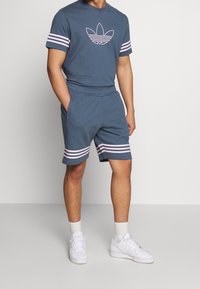 Modrá bavlněná tričko s krátkými rukávy v růžových pruzích a odpovídající šortky s růžovými pruhy na manžetách. Bílé tenisky, volný střih.