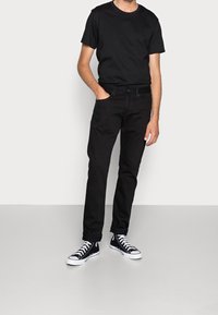 Camiseta de algodón negra combinada con vaqueros de mezclilla negros, con ajuste slim. El calzado incluye zapatillas altas negras con cordones blancos.