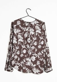 Braune Bluse mit floralem Muster, die ein zartes weißes Blumenmuster, lange Ärmel, einen runden Ausschnitt und eine glatte Textur aufweist, angezeigt auf einem Kleiderbügel.