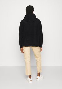 Sort fleece-pullover med hætte, der har en tekstureret overflade. Kombineret med beige cargo-bukser og hvide sneakers med farvekatricer.