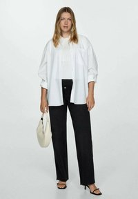White oversized shirt, ribbed white top, high-waisted black jeans, black heeled sandals, holding a cream handbag. Simple and modern design.