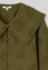Blouse vert olive avec grands motifs floraux brodés, large col à volants et boutons recouverts de tissu sur le devant.