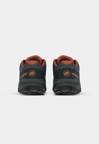 Črne in oranžne MAMMUT pohodniške čevlje z teksturirano zgornjim delom, oblazinjenim ovratnikom in logotipom na peti. Oblikovanje, osredotočeno na vzdržljivost.