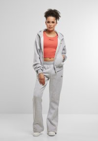 Šedá mikina na zips a zodpovedajúce nohavice vyrobené z mäkkej tkaniny, spojené s priliehavým koralovým crop topom. Oblečenie obsahuje vyšívané logo.