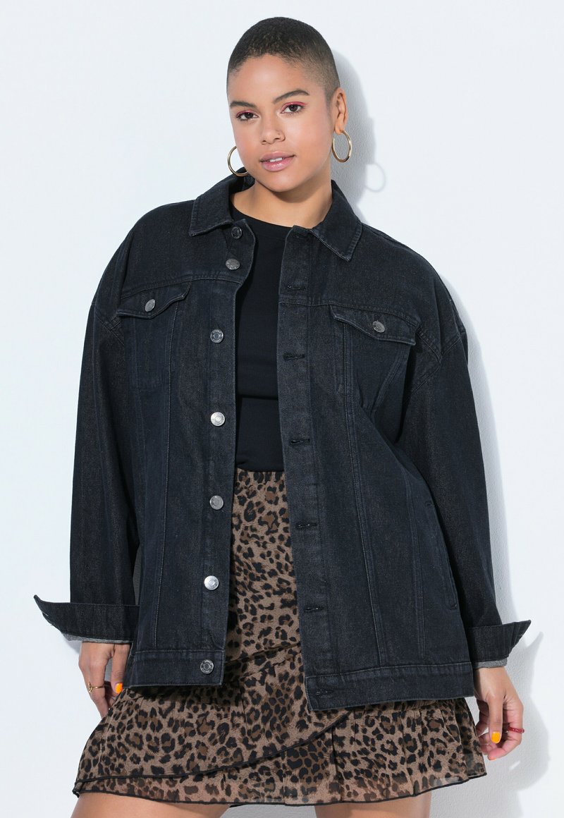 Ung kvinde med kort hår iført guldringøreringe, oversized sort denimjakke, sort top og nederdel med leopardprint.