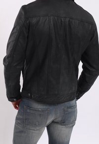 Černá kožená bunda s fitted siluetou, vertikálními švy a patentkami. V kombinaci se světle modrými opranými džíny.
