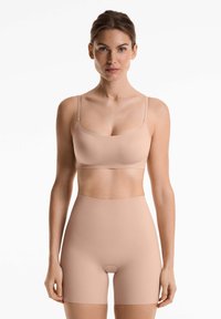 Jasnobeżowy, bezszwowy biustonosz i szorty z wysokim stanem, wykonane z gładkiego materiału, z cienkimi ramiączkami i minimalistycznym wzornictwem.