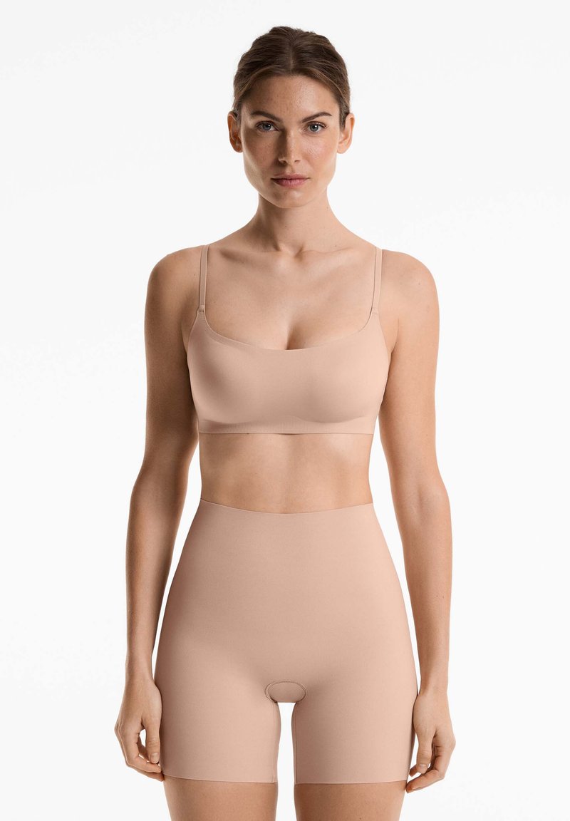 Jasnobeżowy, bezszwowy biustonosz i szorty z wysokim stanem, wykonane z gładkiego materiału, z cienkimi ramiączkami i minimalistycznym wzornictwem.