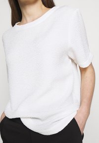 Vit texturerad t-shirt med kort ärm och lös passform, med rund halsringning och en något krökt nederkant.