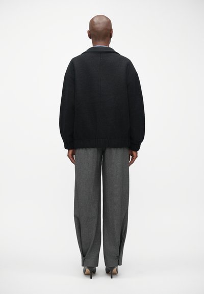 Cárdigan de punto gris oscuro con un ajuste relajado, con dobladillo acanalado y mangas anchas. Combina con pantalones de cuadros en tonos carbón de cintura alta.