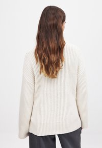 Hellbeige gestrickter Pullover mit lockerer Passform, gerippter Textur, überschnittenen Schultern und einem leicht längeren Rückensaum.