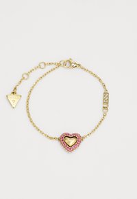 Brățară din lant de aur cu un charm în formă de inimă cu pietre prețioase roz, gravată cu "Guess", și o eticheta triangulară cu logo-ul "Guess".