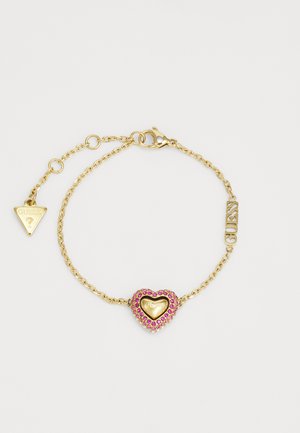 Zlatý náramok s reťazou so srdiečkovým príveskom s ružovými drahokamami, gravírovaným nápisom "Guess", a trojuholníkovou visačkou s logom "Guess".