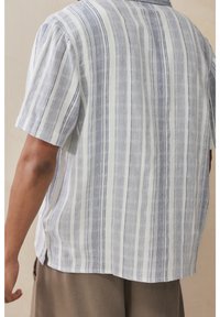 Koszula z krótkim rękawem wykonana z lekkiego materiału z pionowymi, niebiesko-białymi paskami, lekko luźnym krojem oraz rozcięciami po bokach na dole.