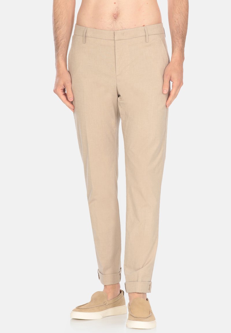 Pantaloni in lino beige con vestibilità tailored, caratterizzati da una texture morbida, tasche laterali e orli arrotolati, abbinati a scarpe slip-on chiare.
