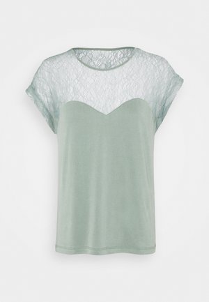 Lys grøn T-shirt med blondeoverlay ved skuldrene, rund halsudskæring og korte ærmer. Har et bølget blonde mønster øverst.