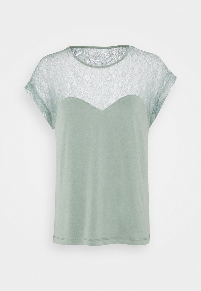 Svetle zelené tričko s krajkovou vložkou na ramenou, kulatým výstřihem a krátkými rukávy. Na vrchní části se nachází krajkový vzor s cik-cak okrajem.