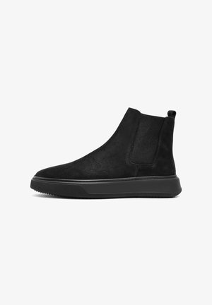 Zwarte suède enkelboots met elastische zijpanelen, ronde neus en rubberen zool. Voorzien van een gestructureerd patroon en een kleine trekband aan de achterkant voor eenvoudig aan- en uittrekken.