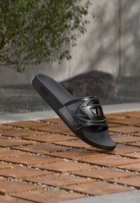 Șapcă neagră de cauciuc moale cu un design elegant, având o curea proeminentă cu accente decorative. Talpă texturată.