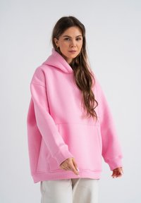 Hoodie oversize rosa realizzato in morbido tessuto con tasca frontale a marsupio, polsini a costine e cappuccio foderato. Design semplice e rilassato.