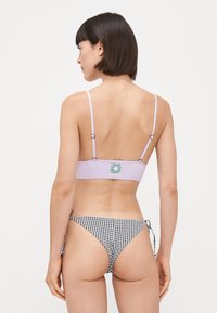 Haut de bikini lilas avec des fines bretelles ajustables et un logo floral ; associé à un bas de bikini à carreaux noir et blanc avec des liens sur les côtés.