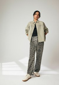 Alavijų žalios spalvos marškiniai su franžo detalėmis, juodas viršus ir leopardų rašto plačios kojos kelnės, derintos su šviesiomis sportinėmis bateliais.