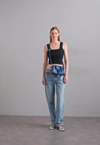 Kék crossbody táska texturált felülettel, állítható pánttal és cipzárral. Fekete felsővel viselve és világoskék farmerral párosítva.