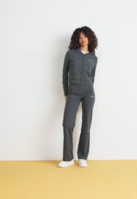 Szürke sportos tréningruha cipzáras kapucnis dzsekivel és illő nadrággal, puha anyagból készült. A fehér sportcipő teszi teljessé az outfitet.