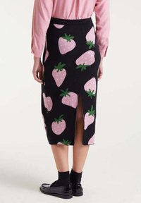 Falda midi negra con patrones de fresas rosas, con abertura trasera, llevada con medias negras, mocasines negros y una camiseta de manga larga rosa.