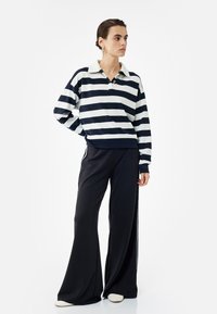 Polo de rayas en azul marino y blanco con manga larga y cuello, combinado con pantalones amplios negros y zapatos blancos. Tela texturizada con detalles de botones.