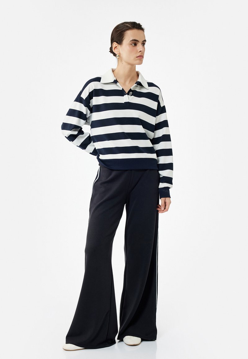 Polo de rayas en azul marino y blanco con manga larga y cuello, combinado con pantalones amplios negros y zapatos blancos. Tela texturizada con detalles de botones.