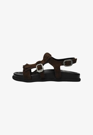 Brown suede flat sandal with two silver buckles and tassel detail on a black sole, side view on white background.