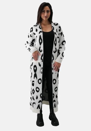 Langer, weißer Cardigan mit schwarzem Leopardenmuster, mit gerippten Bündchen und Taschen, über einem schwarzen Outfit getragen, detaillierte Textur sichtbar.