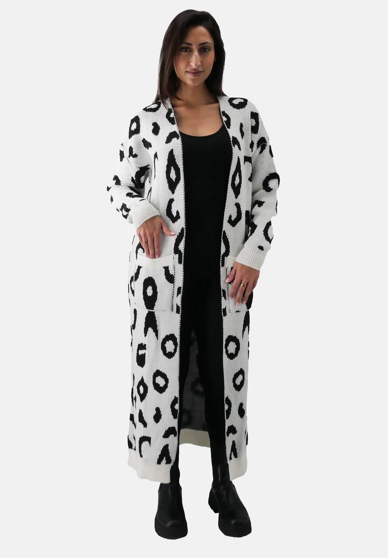 Langer, weißer Cardigan mit schwarzem Leopardenmuster, mit gerippten Bündchen und Taschen, über einem schwarzen Outfit getragen, detaillierte Textur sichtbar.