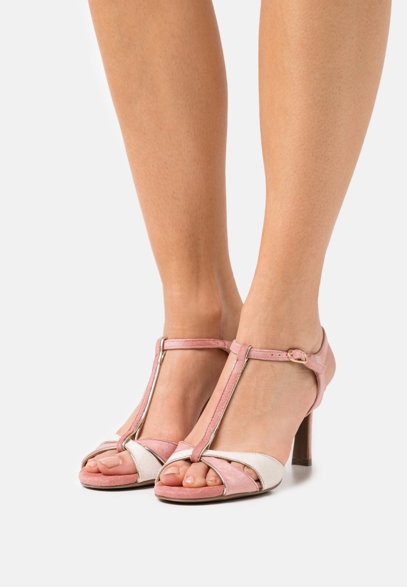 Sandales à talons hauts en cuir rose et blanc avec un design à lanière en T, bout ouvert et texture lisse. Présentent un talon fin et une boucle à la cheville.