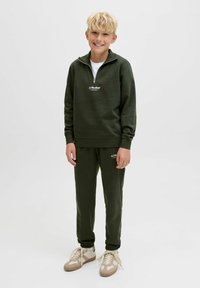 Grön zip-up sweatshirt med en vit logo, matchande gröna joggers. Skorna är beige med snören. Enkel, sportig design.