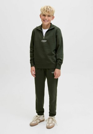 Grüner Reißverschluss-Sweatshirt mit einem weißen Logo, kombiniert mit passenden grünen Jogginghosen. Die Sneakers sind beige mit Schnürsenkeln. Einfaches, sportliches Design.