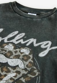 Close-up of dark gray t-shirt with faded white cursive text and a leopard print cat wearing white sunglasses graphic.