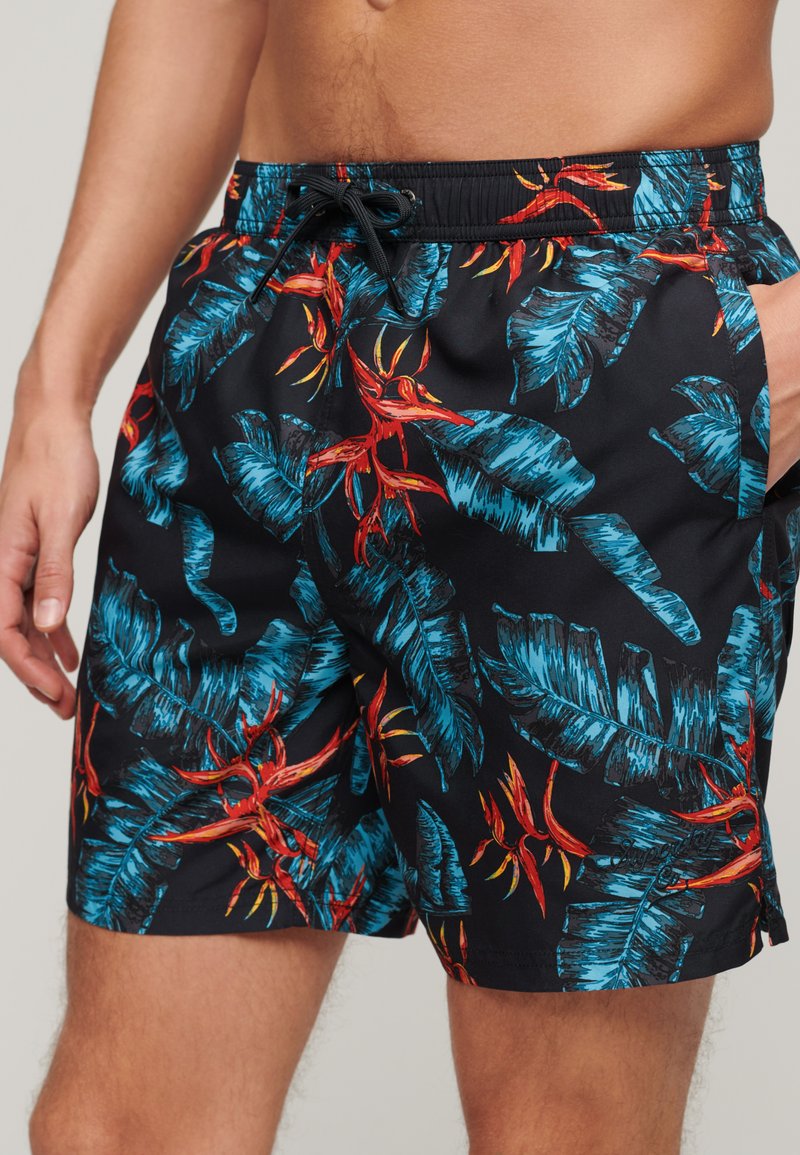 Costume da bagno neri con un vivace motivo tropicale di foglie e fiori blu e rossi, dotati di una cintura elastica e tasche laterali.