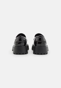 Chaussures en cuir verni noir avec une semelle épaisse, présentant une surface lisse et des détails de couture subtils sur le talon et le dessus.